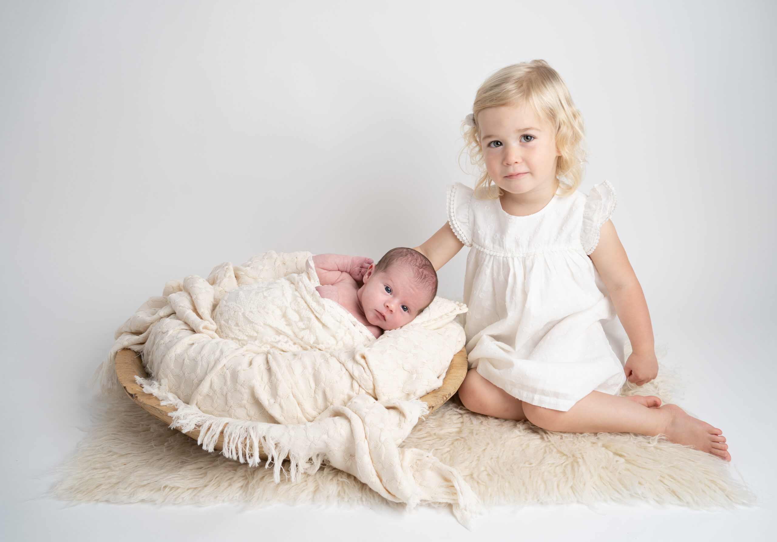 newborn baby in a basket with her sister kneeling by